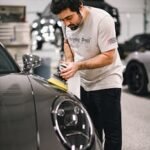 Man carefully polishing a sleek sports car in a well-lit garage, focused on detailing.