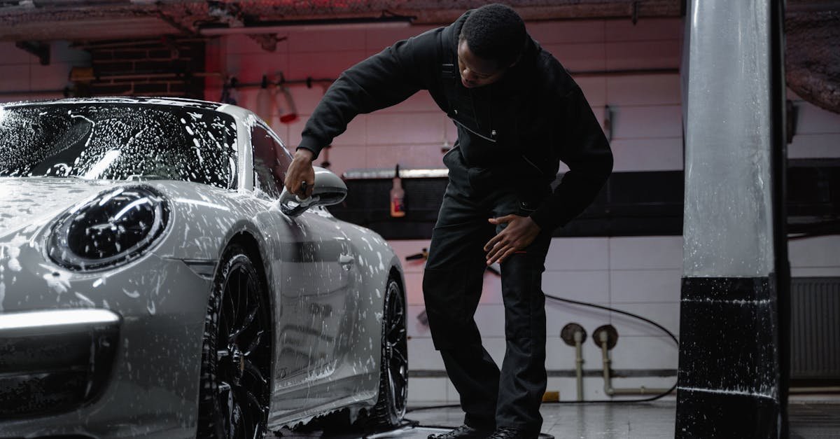 Man washing a luxury car in an indoor garage, emphasizing automotive care.