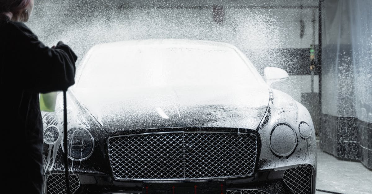 Black luxury car receiving a foamy wash in an indoor car wash service.