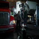 Mechanics performing truck maintenance and repair in an indoor garage setting.