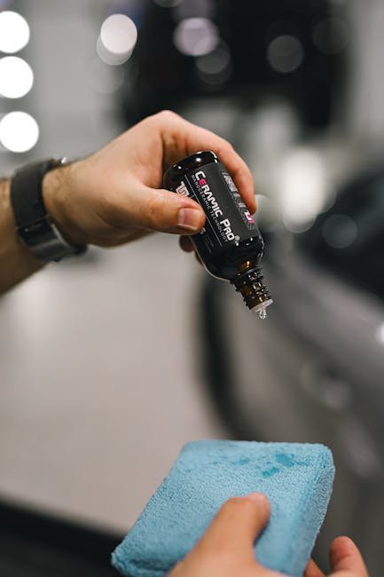 Close-up of hands applying ceramic coating on car with blue sponge.