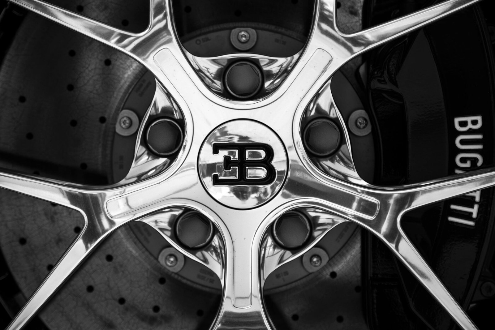 Black and white close-up shot of a Bugatti car rim showing intricate design and luxury branding.