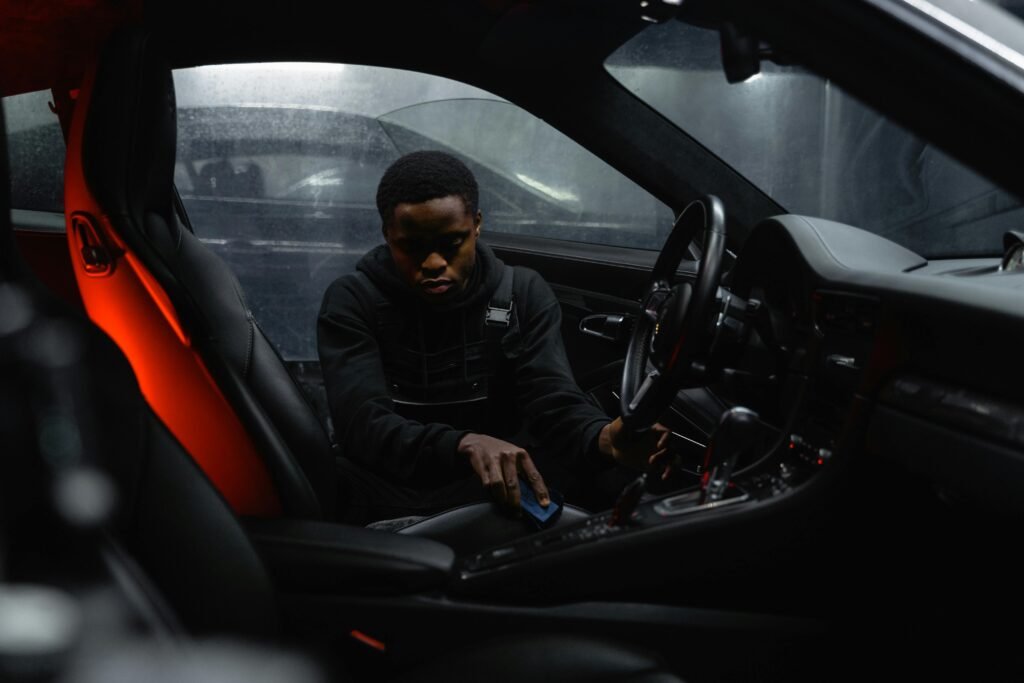 Man meticulously cleaning inside a luxury car with a focus on interior design and ambiance lighting.